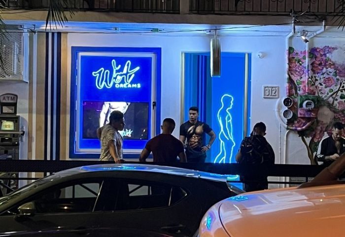 Night view of Wet Dreams gay bar in Puerto Vallarta. Men gather outside the bar with blue neon sign and male silhouette. Gay travel.