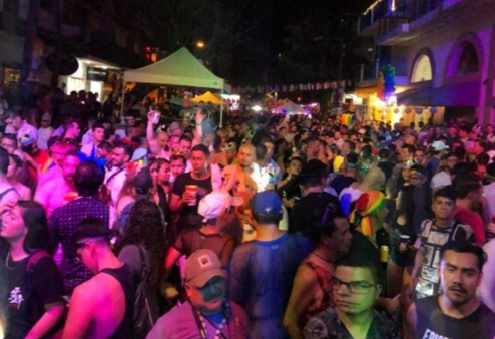 Crowd at a wet gay bar in Puerto Vallarta, Mexico. Nightlife scene with many people, tents, and rainbow flags. Gay travel destination.