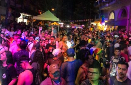 Crowd at a wet gay bar in Puerto Vallarta, Mexico. Nightlife scene with many people, tents, and rainbow flags. Gay travel destination.