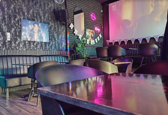 Interior of Why Not Cafe and Bar, Budapest. Stylish seating, dark walls, neon lights, and a large screen create a vibrant, gay-friendly atmosphere.