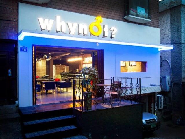 Why Not Cocktail Bar, a gay bar. The entrance of the bar has a sign with the male symbol. Interior view with tables and chairs. Gay travel.