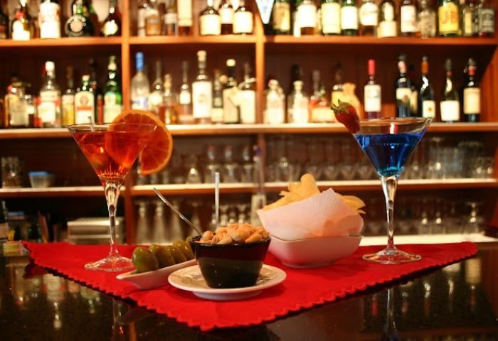 Why Not? Gay Bar in Madrid: Cocktails, olives, nuts, and chips are on the bar at this gay-friendly travel destination. Shelves of liquor behind.