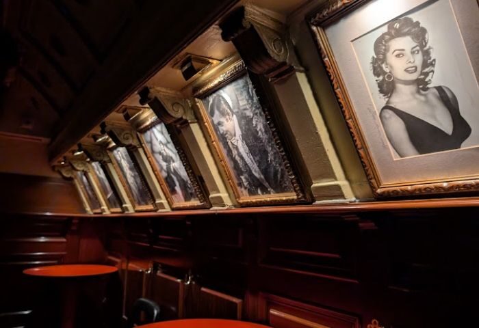 Interior of Why Not? gay bar in Madrid. Framed black and white portraits line the wall above red tables. Gay travel advice.