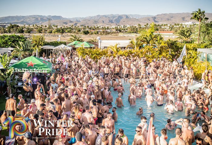 Gay Gran Canaria Travel: Winter Pride 2024 pool party. A large crowd of gay men enjoy the sun and water during the Maspalomas event.