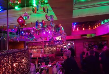Interior of Woody's and Sailor gay bar in Toronto. Colorful lights, patrons at the bar, and hanging decorations. Gay travel.