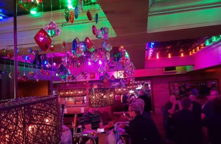 Interior of Woody's and Sailor gay bar in Toronto. Colorful lights, patrons at the bar, and hanging decorations. Gay travel.