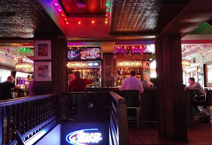 Interior of Woody's gay bar in Toronto. People at the bar, colorful lights, and a Bud Light neon sign. Gay travel advice.