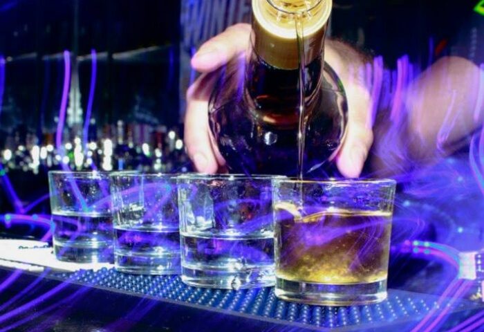 Bartender pouring shots at Woof X Lisbon, a gay bar. Lisbon nightlife, gay travel advice. Purple neon lights.