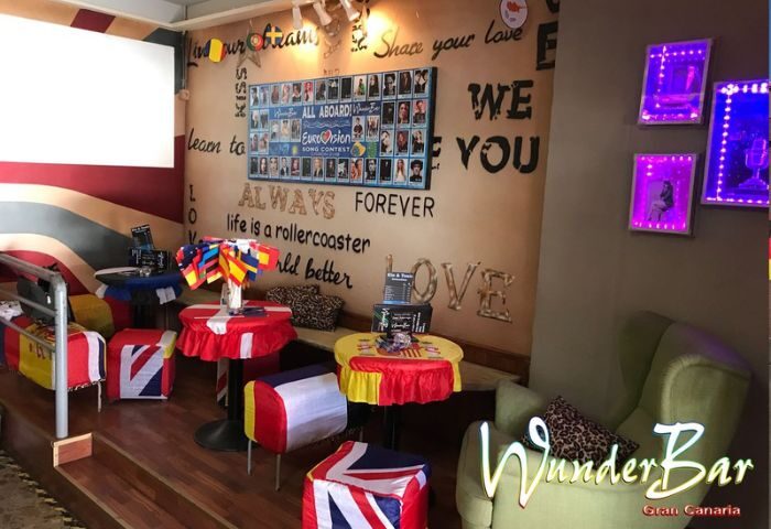 WunderBar gay bar interior in Gran Canaria. Tables with flags, Eurovision art, and a cozy corner. A vibrant gay travel destination.