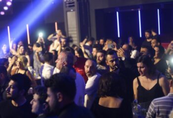 Crowded X Large Club Istanbul scene. People dancing, taking photos, and enjoying the gay nightlife scene. Blue lighting.
