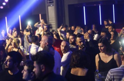 Crowded X Large Club Istanbul scene. People dancing, taking photos, and enjoying the gay nightlife scene. Blue lighting.
