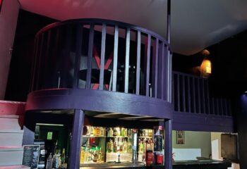 XXL Club Lisbon interior. Two-story bar area with purple railings and a fully stocked bar. Gay travel advice for Lisbon nightlife.