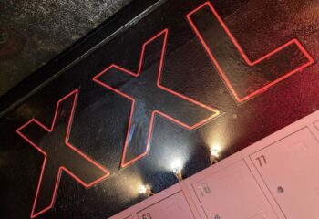 XXL Gay Cruise Club in Torremolinos sign. The sign is black with red trim and is located above a row of pink lockers.