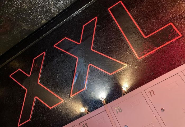 XXL Gay Cruise Club in Torremolinos sign. The sign is black with red trim and is located above a row of pink lockers.