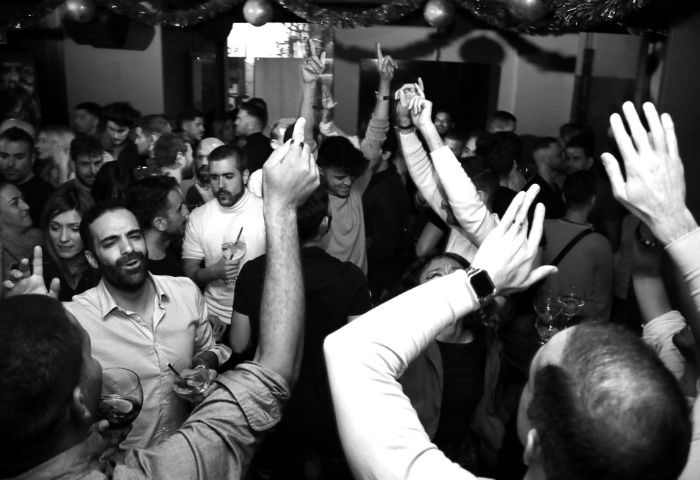 Black and white shot of crowded YOUME Gay Bar in Madrid. People are dancing with their hands in the air, enjoying the gay nightlife.