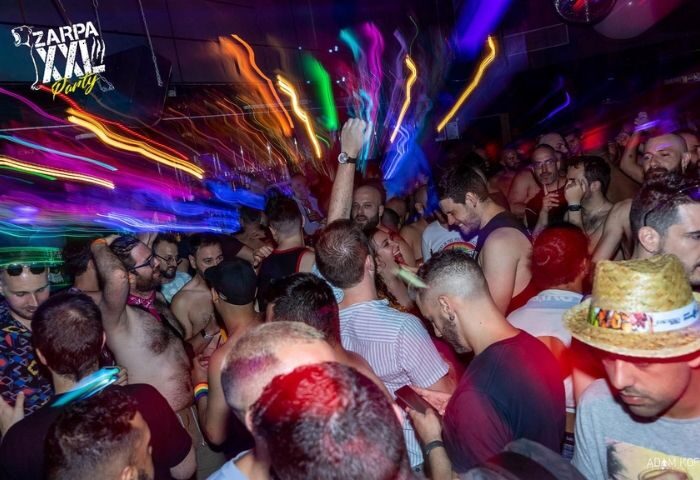 Crowded Zarpa Bear de Copas gay bar in Madrid. Gay nightlife scene with many men, colorful lights, and party atmosphere.