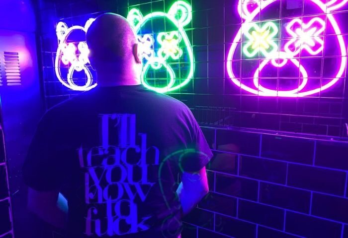 Man in Zarpa Bear de Copas gay bar, Madrid. Neon bear lights. Gay travel advice. Nightlife. Dark t-shirt with bold text. Fun, edgy vibe.