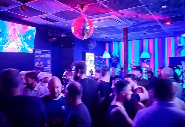 Inside Zarpa Bear de Copas, a gay bar in Madrid. Crowd of men under disco ball and neon lights. Gay nightlife, travel.