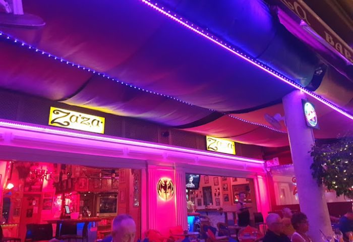 Zaza Bar, a gay bar in Gran Canaria, Spain. Exterior view with pink and purple lighting, showing the bar's signage and outdoor seating.