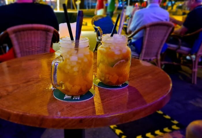 Two cocktails at Zaza Bar, a gay bar in Gran Canaria. Drinks with ice and straws sit on a wooden table, inviting gay travelers.
