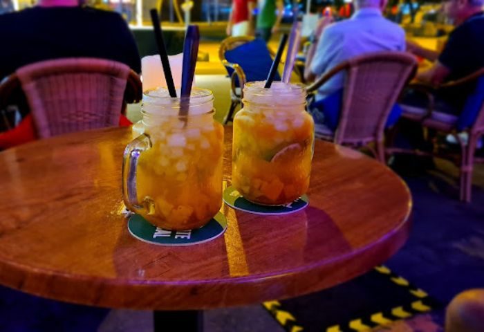 Two cocktails at Zaza Bar, a gay bar in Gran Canaria. Drinks with ice and straws sit on a wooden table, inviting gay travelers.