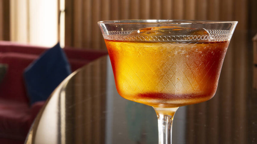 Cocktail at Ziggy's Gay Bar. Close-up of a stemmed glass filled with an amber-colored drink and ice, on a reflective table. Gay travel.