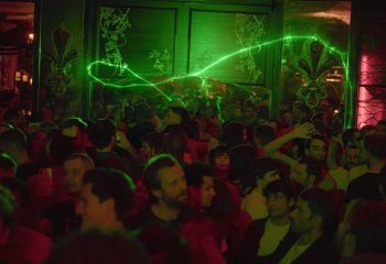 Crowd at a gay bar in Paris with green laser lights. Nightlife scene related to Bizarre Love Triangle gay travel advice.