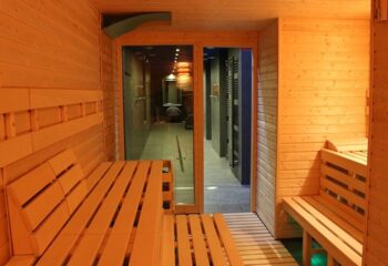 Sauna Bonbon: Interior view of a wooden sauna with benches, leading to a shower area. Gay travel spa experience.