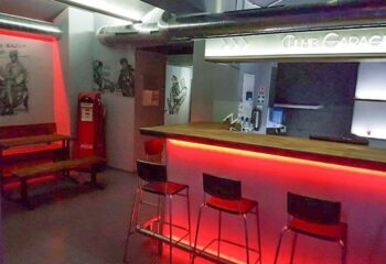 Interior of Club Garage, a gay bar: red lighting, bar stools, vintage gas pump, and artwork. A travel destination for gay men.