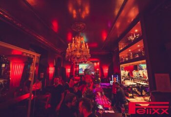 Interior of Felixx Bar, Vienna, a gay bar, featuring a chandelier, red lighting, and patrons. Nightlife scene for gay men traveling.