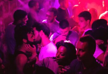 Freedj Paris: Gay men kissing in a crowded club with purple lighting. Nightlife scene in Paris, France. Gay travel destination.