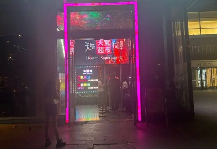 Entrance to Heaven Beer Bar, a gay nightlife spot. Neon lights frame the door. People queue to enter. The bar's sign is visible. image.jpg