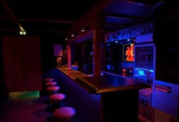 Le Keller, Paris: Interior of a gay bar, featuring a long bar with stools, illuminated with red and blue lights, creating a vibrant atmosphere.