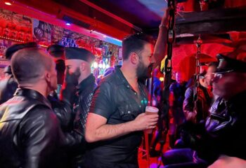 Le Mensch Paris: Gay men in leather attire at a bar. Fetish scene with men in caps, vests, and harnesses. Nightlife in Paris for gay travelers.