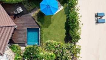 Aerial view of SAii Koh Samui Villas room 0084. Features a private pool, wooden deck, blue umbrella, lush garden, and beach access for gay travelers.