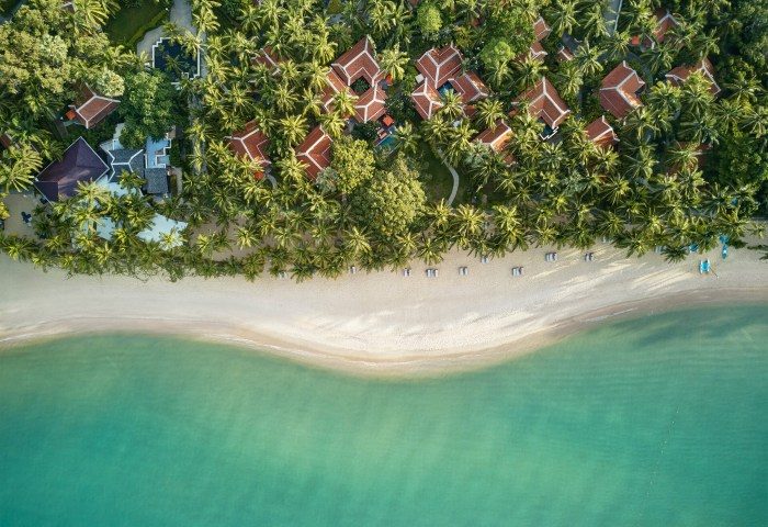 Aerial view of Santiburi Beach, Koh Samui. White sand, turquoise water, palm trees, and resort buildings. Perfect for gay men's travel advice.