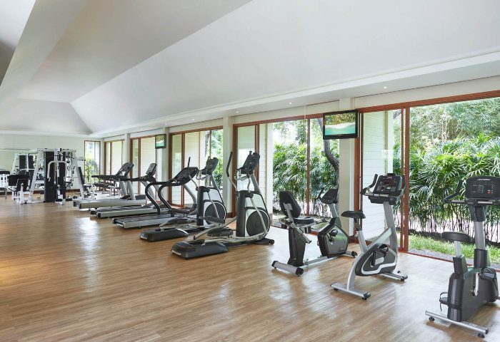 Santiburi Koh Samui's sports center: Treadmills, ellipticals, and stationary bikes face lush greenery. Fitness and wellness for gay travelers.
