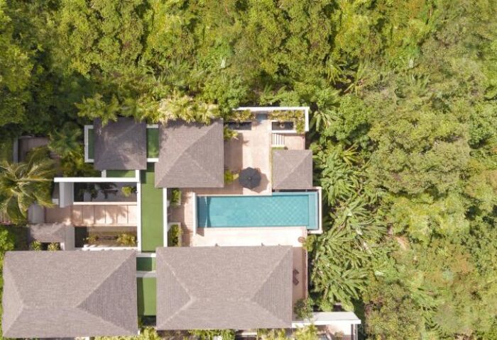 Aerial view of The Pavilions Phuket villa. Pool, rooftops, and lush greenery. Luxury gay travel destination.