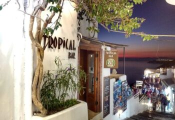 Exterior of Tropical Bar at dusk, a gay travel destination. Whitewashed building, ocean view, and a crowd of people. Perfect for gay nightlife.
