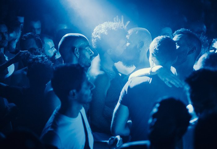 VendrediX Paris: Gay men dancing at a dark club. Two men kissing. Nightlife scene with blue lighting. Gay travel advice for Paris.